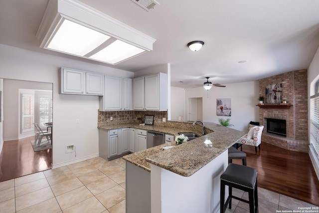 kitchen with a sink, a peninsula, dishwasher, light tile patterned floors, and ceiling fan