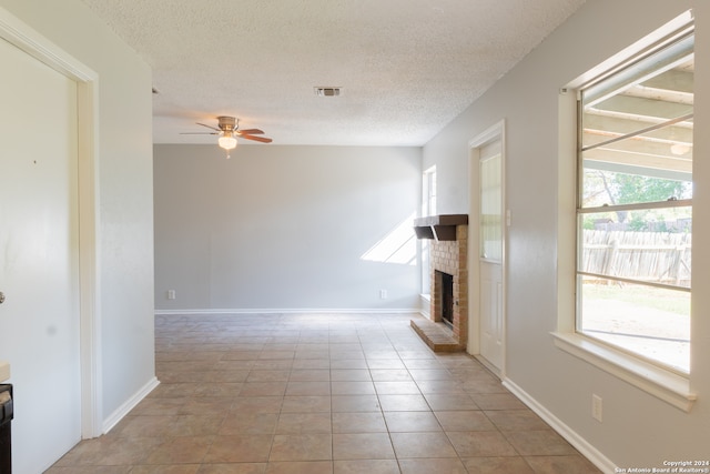 unfurnished living room with a fireplace, a textured ceiling, ceiling fan, and light tile patterned flooring