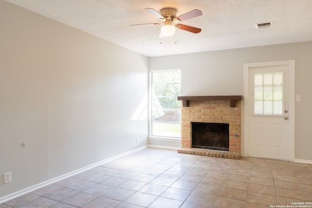 unfurnished living room featuring light tile patterned floors, a textured ceiling, a brick fireplace, and plenty of natural light