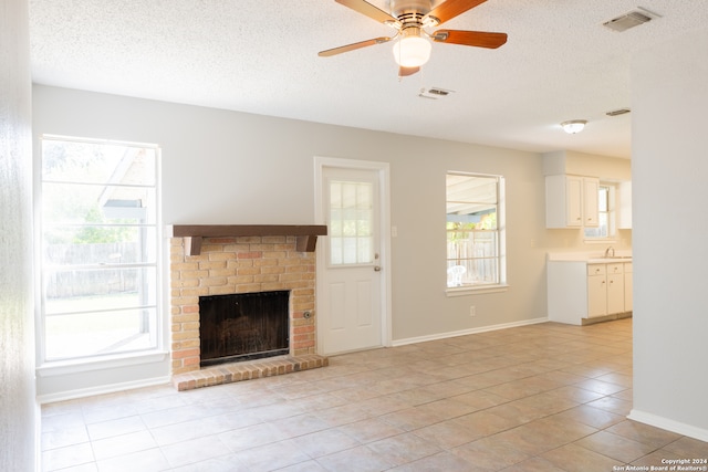 unfurnished living room featuring ceiling fan, sink, a textured ceiling, a fireplace, and light tile patterned floors