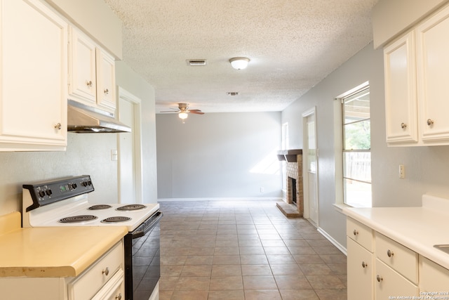 kitchen featuring a brick fireplace, ceiling fan, white electric stove, white cabinets, and light tile patterned flooring