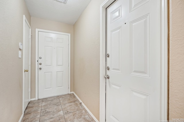 doorway with a textured ceiling and light tile patterned flooring