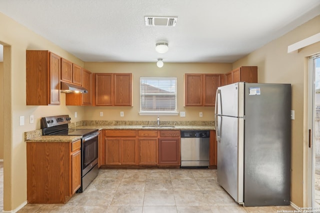 kitchen featuring appliances with stainless steel finishes, light stone counters, a textured ceiling, sink, and light tile patterned floors