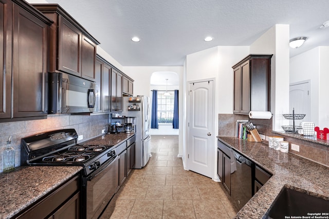 kitchen featuring appliances with stainless steel finishes, tasteful backsplash, dark brown cabinetry, a textured ceiling, and dark stone countertops