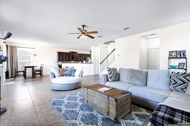 tiled living room with ceiling fan with notable chandelier