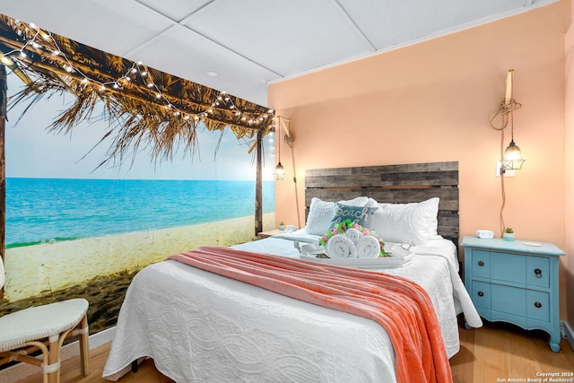 bedroom featuring a water view, a drop ceiling, a beach view, and hardwood / wood-style flooring