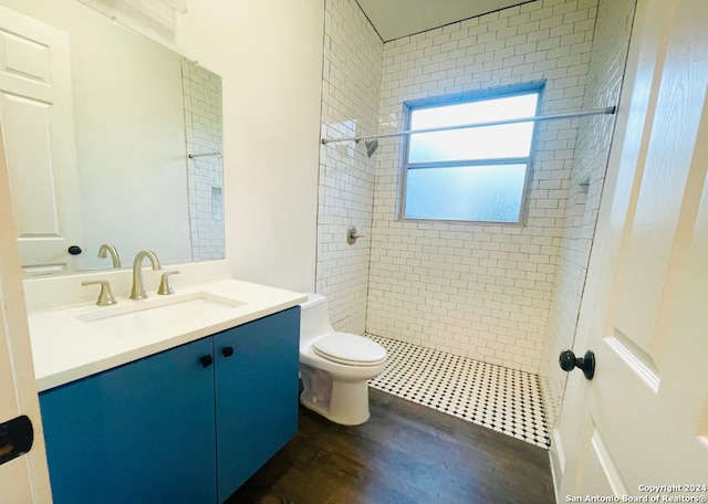 bathroom with a tile shower, vanity, hardwood / wood-style flooring, and toilet