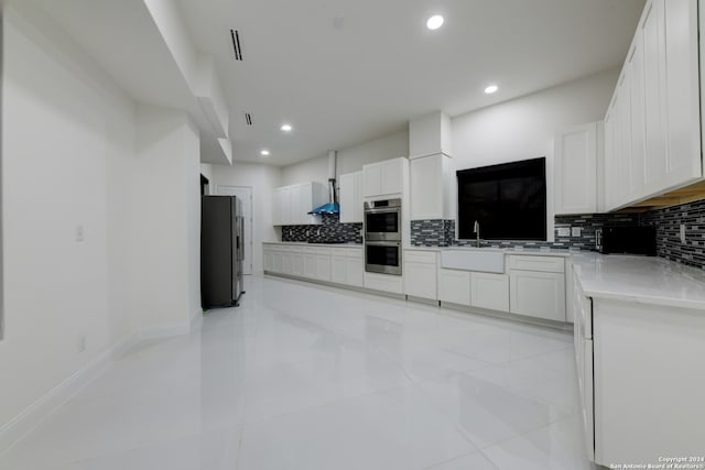 kitchen with tasteful backsplash, white cabinetry, stainless steel appliances, and wall chimney range hood