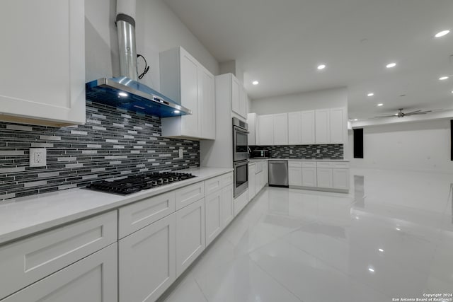 kitchen with tasteful backsplash, white cabinets, wall chimney range hood, and appliances with stainless steel finishes