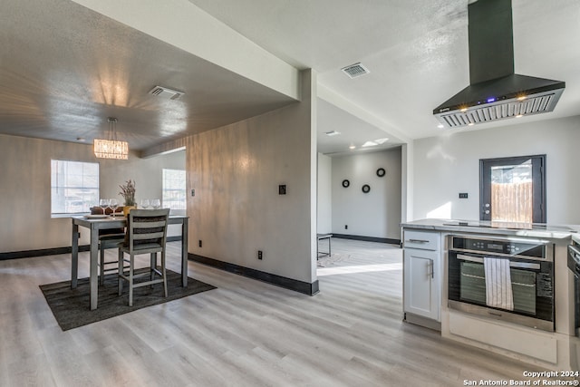 interior space featuring stainless steel oven, light hardwood / wood-style flooring, range hood, a textured ceiling, and white cabinets