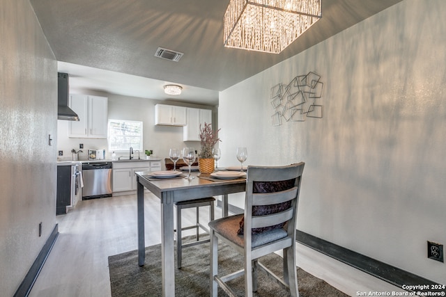 kitchen with light wood-type flooring, stainless steel dishwasher, sink, wall chimney range hood, and white cabinetry