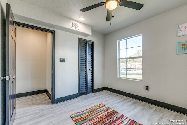 unfurnished bedroom with a textured ceiling, light wood-type flooring, a closet, and ceiling fan