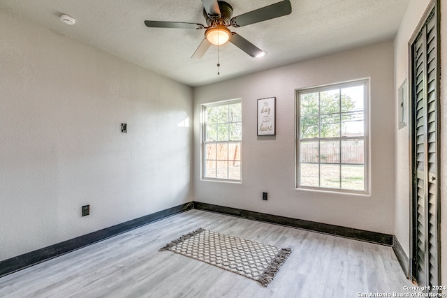 empty room featuring a textured ceiling, light hardwood / wood-style flooring, a wealth of natural light, and ceiling fan