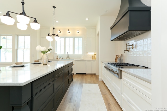 kitchen with custom exhaust hood, white cabinets, hanging light fixtures, light wood-type flooring, and a healthy amount of sunlight