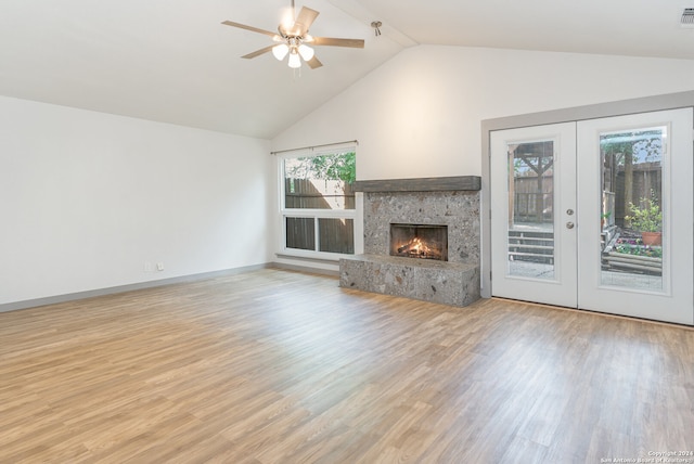 unfurnished living room featuring french doors, light wood-type flooring, ceiling fan, a stone fireplace, and lofted ceiling