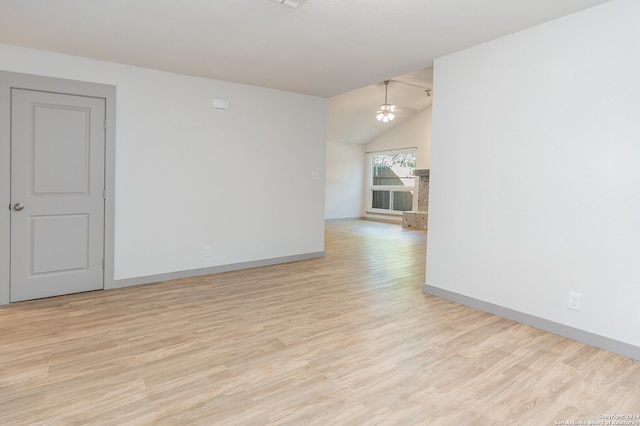 empty room with a chandelier, light wood-type flooring, and vaulted ceiling