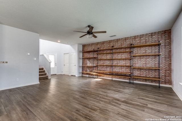 unfurnished living room with dark hardwood / wood-style floors, ceiling fan, and brick wall