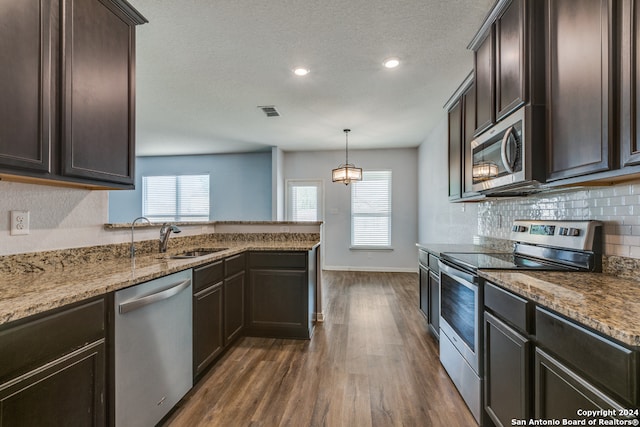 kitchen with sink, dark wood-type flooring, stainless steel appliances, decorative light fixtures, and dark brown cabinets