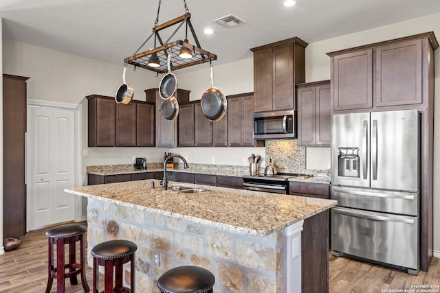 kitchen with light wood-type flooring, stainless steel appliances, a center island with sink, and sink