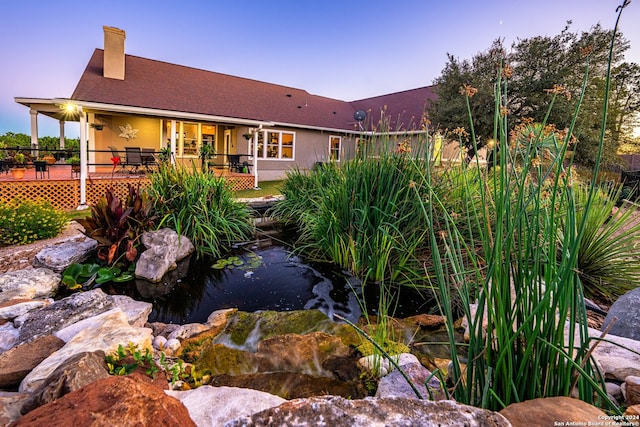 back of property featuring a garden pond and a wooden deck