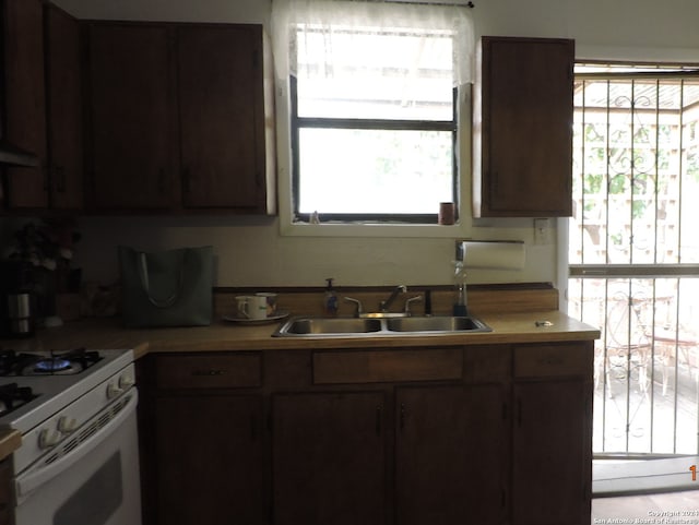 kitchen with dark brown cabinetry, sink, and white gas range oven