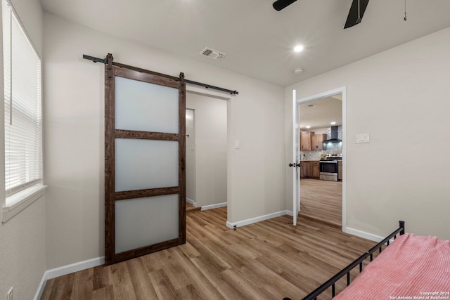 bedroom featuring light wood-type flooring, a barn door, and ceiling fan