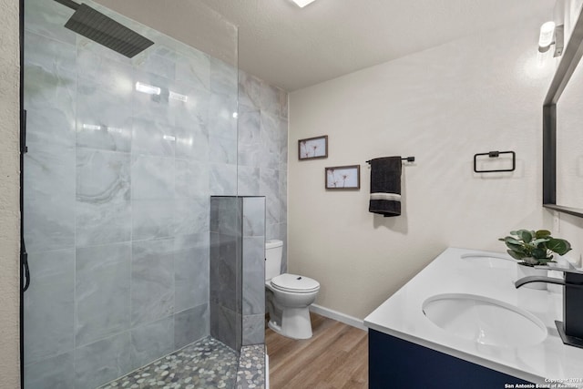 bathroom featuring a tile shower, vanity, a textured ceiling, wood-type flooring, and toilet