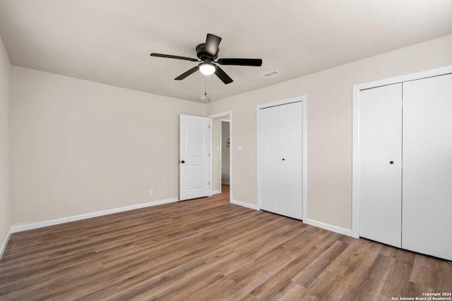 unfurnished bedroom featuring light hardwood / wood-style floors, ceiling fan, and multiple closets