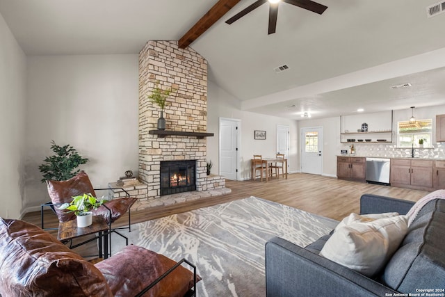 living room with ceiling fan, sink, a stone fireplace, vaulted ceiling with beams, and light hardwood / wood-style flooring