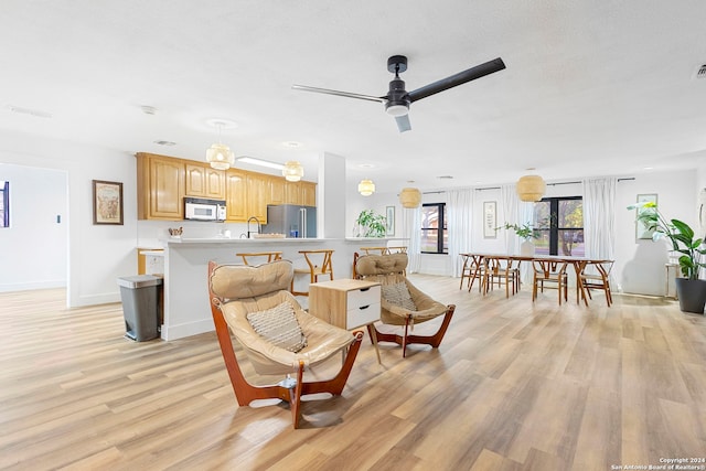 living room with ceiling fan, sink, a textured ceiling, and light wood-type flooring