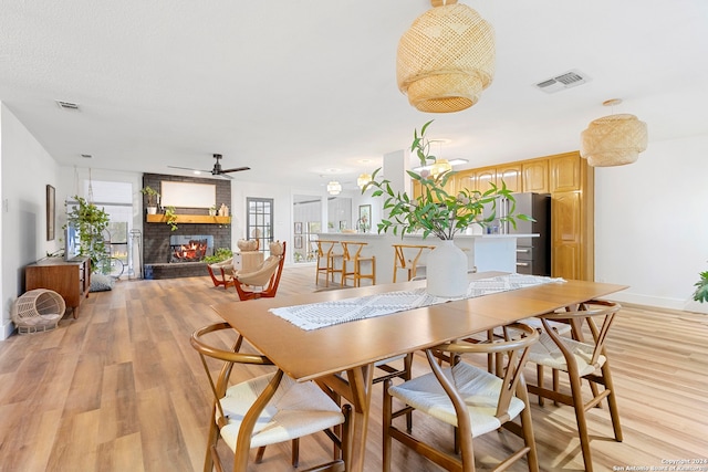 dining area with light hardwood / wood-style floors, a brick fireplace, and ceiling fan