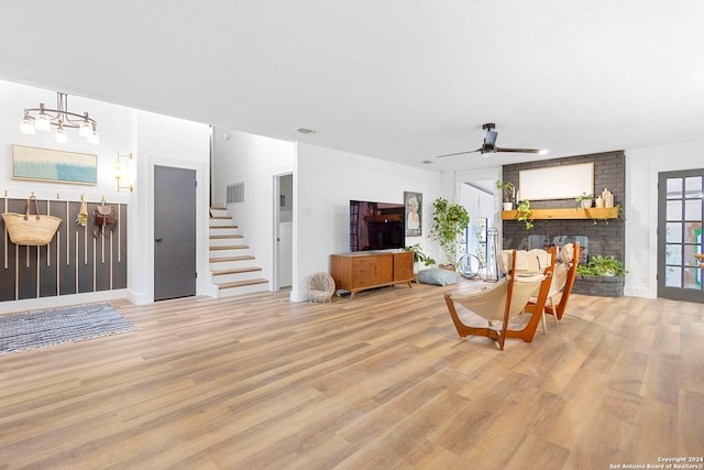 living room with ceiling fan with notable chandelier, light wood-type flooring, and a fireplace