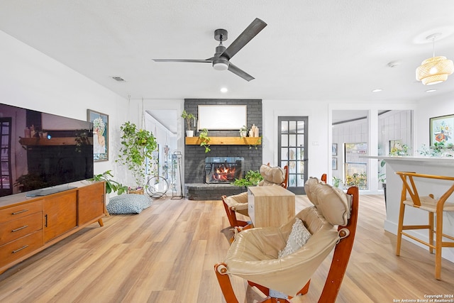 living room with ceiling fan, a fireplace, light hardwood / wood-style floors, and a textured ceiling