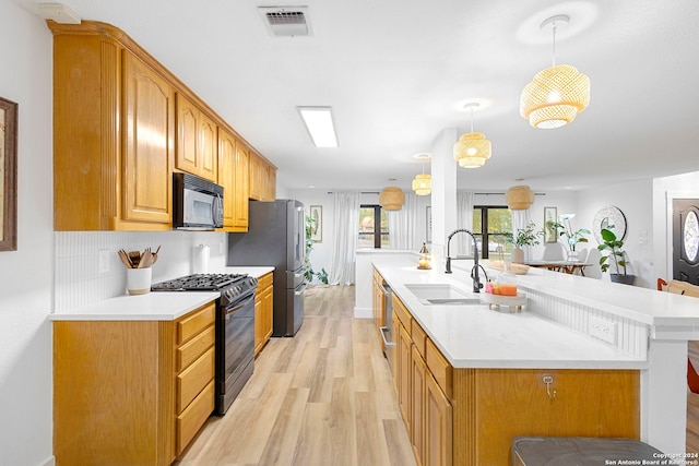 kitchen featuring pendant lighting, black appliances, sink, tasteful backsplash, and light hardwood / wood-style floors