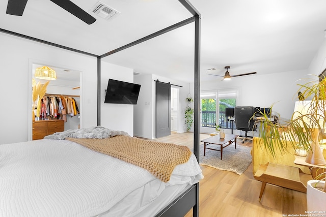 bedroom featuring access to exterior, light wood-type flooring, a barn door, a spacious closet, and a closet