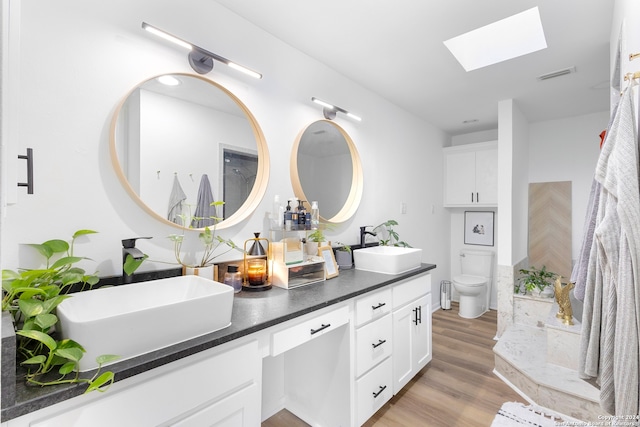 bathroom featuring wood-type flooring, vanity, a skylight, and toilet