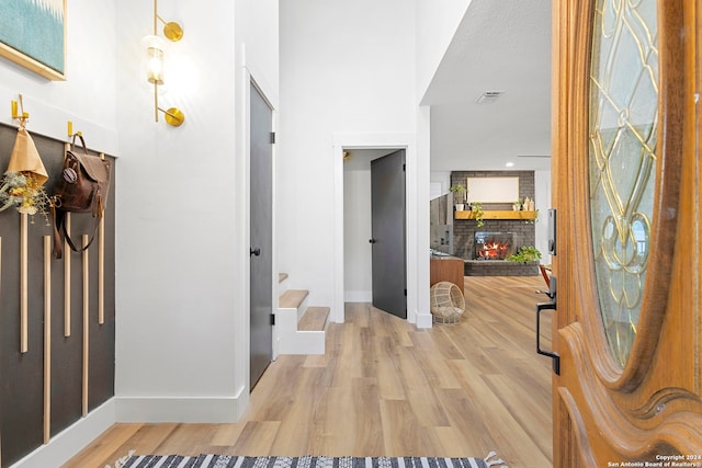 entrance foyer featuring hardwood / wood-style floors, a textured ceiling, a brick fireplace, and a high ceiling