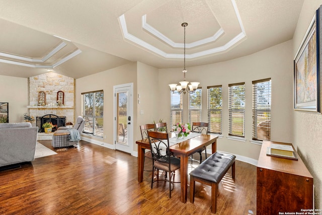 dining room with a stone fireplace, dark wood-type flooring, a healthy amount of sunlight, and an inviting chandelier