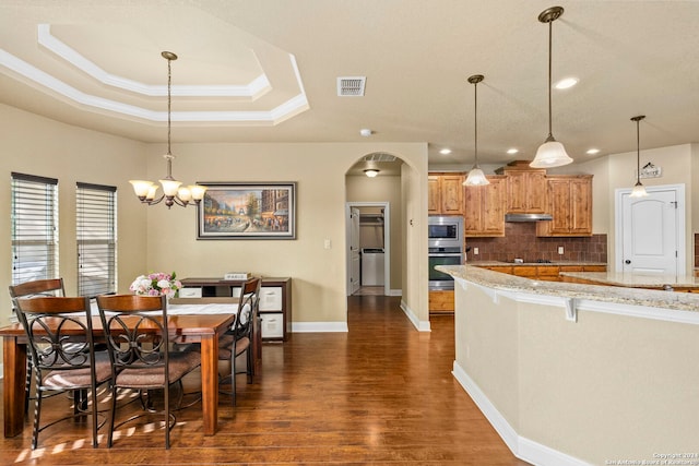 kitchen featuring pendant lighting, a breakfast bar, dark wood-type flooring, decorative backsplash, and light stone countertops