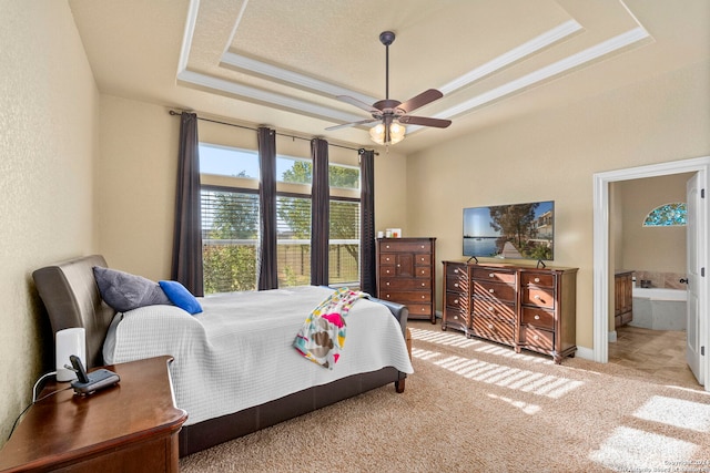 bedroom featuring light carpet, ensuite bathroom, ceiling fan, ornamental molding, and a tray ceiling