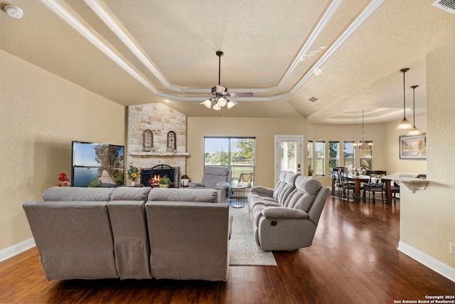 living room featuring ceiling fan, dark hardwood / wood-style flooring, a textured ceiling, a tray ceiling, and a fireplace