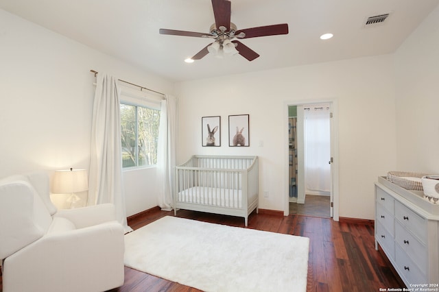 bedroom with ceiling fan, a nursery area, and dark hardwood / wood-style floors