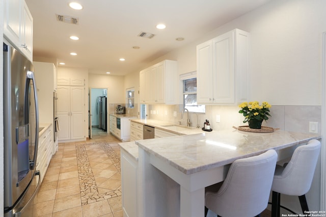 kitchen featuring sink, kitchen peninsula, a breakfast bar area, white cabinets, and appliances with stainless steel finishes