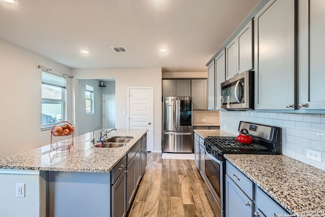 kitchen with a center island with sink, sink, light hardwood / wood-style flooring, light stone countertops, and stainless steel appliances