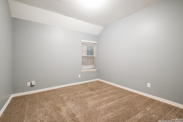 spare room featuring carpet, a textured ceiling, and lofted ceiling