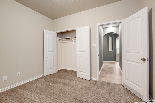 unfurnished bedroom with light carpet, a textured ceiling, and a closet