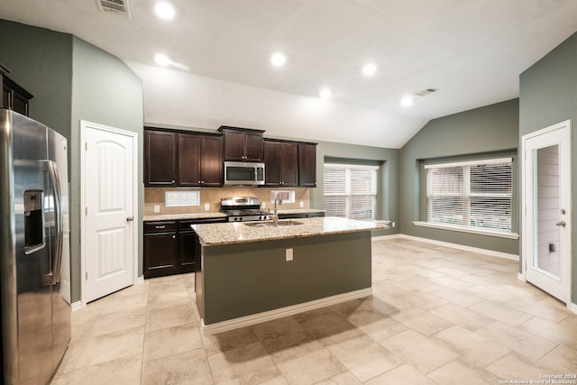 kitchen featuring a kitchen island with sink, lofted ceiling, decorative backsplash, dark brown cabinets, and appliances with stainless steel finishes