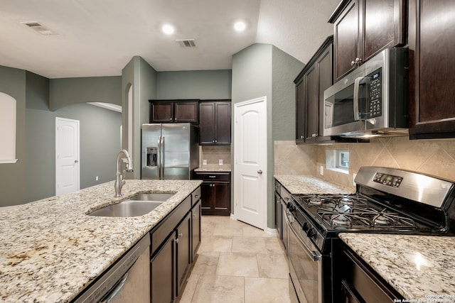 kitchen with sink, light stone counters, decorative backsplash, dark brown cabinets, and appliances with stainless steel finishes