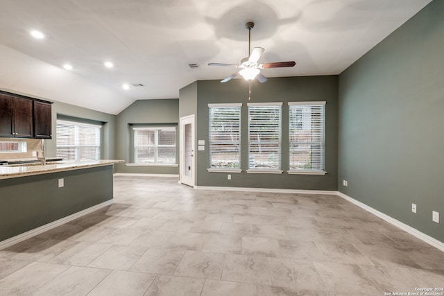 kitchen with lofted ceiling, ceiling fan, light tile patterned floors, dark brown cabinets, and light stone counters