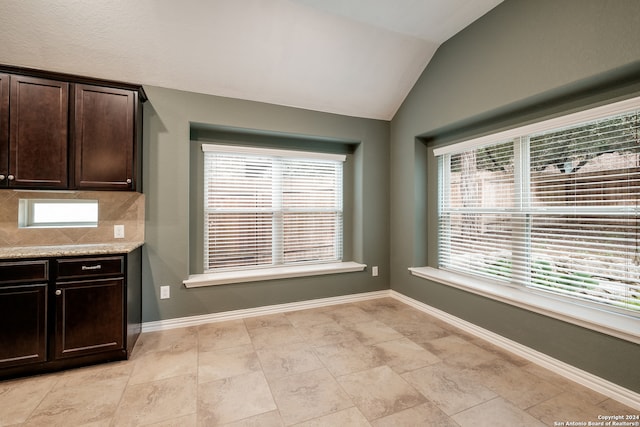 kitchen with tasteful backsplash, light stone countertops, dark brown cabinets, and vaulted ceiling